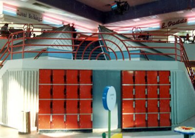 Indoor playground in a mall with geometric climbing structures and colorful lockers, surrounded by store signs and lighting.