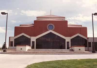 Modern red brick building with a curved roof, large windows, and multiple entrances, set against a cloudy sky.