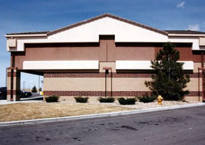 A single-story commercial building with a brown brick facade and tan stucco, featuring a drive-thru window and a small tree in the front.