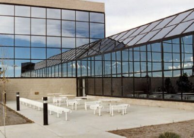 Modern office building with large glass facade, reflecting the clouds and equipped with outdoor white picnic tables.