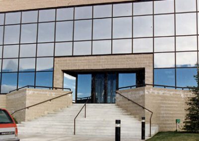 Modern office building with reflective glass facade and a central staircase leading to a double-door entrance.