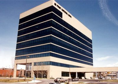 A mid-sized multi-story office building with a black and white facade, marked with "first national bank" on the top, under a clear blue sky.